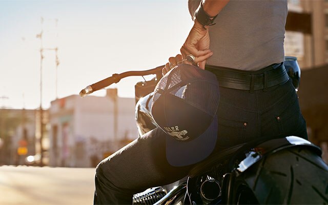 Eine Motorradfahrerin hat in der Detailaufnahme die Cap Boxer aus der Kollektion in der Hand und trägt die Jeans RoadCrafted für Damen.